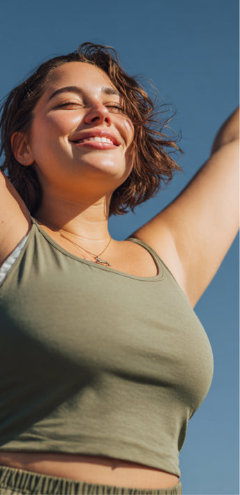 Woman in a green tank top stretching with her arms raised against a blue sky