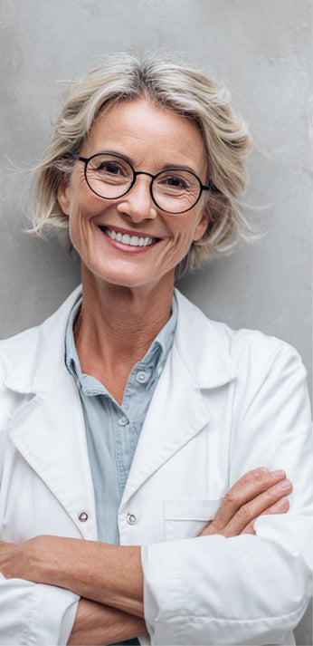 Smiling woman with glasses in a white coat, arms folded